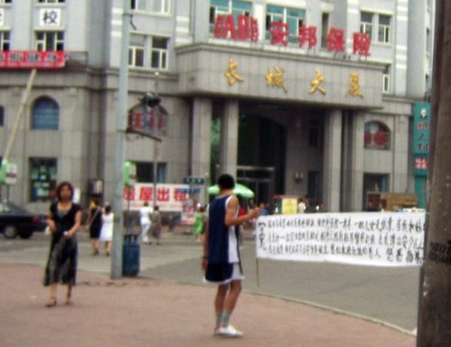 Cao Yang brandissant une banderole demandant la libération de sa mère, pratiquante de Falun Gong persécutée par le  régime chinois, face au Département de police de Jilin.