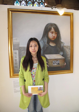 Amy Yu devant le tableau « Les larmes d'une orpheline » à l'exposition internationale L'Art de Zhen Shan Ren (Authenticité-Bienveillance-Tolérance) en juin 2013, tenant une carte postale appelant à secourir son père.
