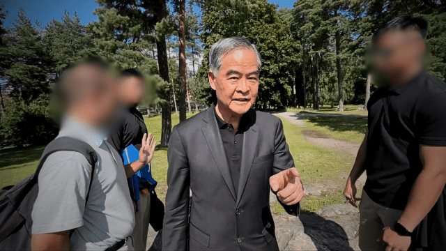 Leung Chun-ying (au centre) aborde et prend verbalement à partie un pratiquant de Falun Gong dans un parc public en Finlande.